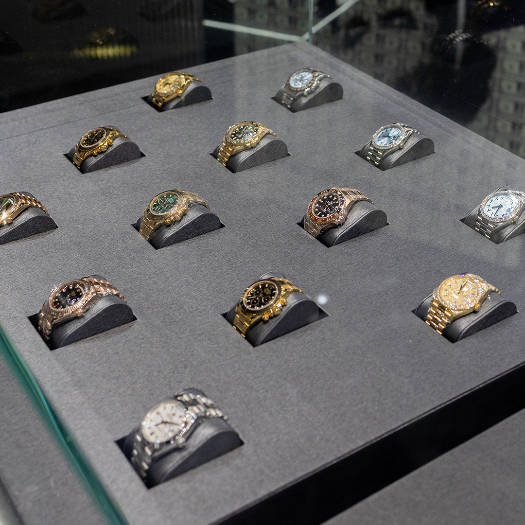 Collection of luxury watches displayed in a glass case, featuring various styles and colors.